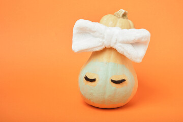Autumn pumpkin with clay mask in white cosmetic bandage on orange background, copy space, mock up
