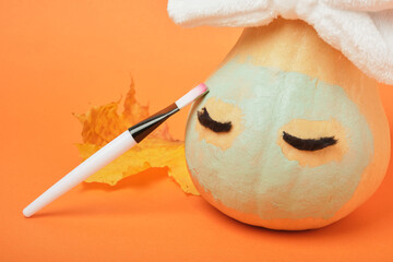 Autumn pumpkin with clay mask in white cosmetic bandage on orange background, brushes for applying mask, copy space, mock up