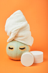 Mock-up jars of cream and yellow pumpkin in a clay mask and a towel on the head Natural organic spa cosmetics concept. Vitamin intense seed of pumpkin cream concept.