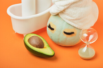 Avocado-based cosmetics concept, pumpkin and various cosmetic containers on orange background, autumn beauty care