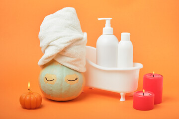 Pumpkins and bottles of cosmetic products on bright orange background, candles and reusable pad, autumn self care
