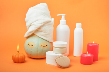Pumpkins and bottles of cosmetic products on bright orange background, candles and reusable pad, autumn self care