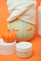 Mock-up jars of cream and yellow pumpkin in a clay mask and a towel on the head Natural organic spa cosmetics concept. Vitamin intense seed of pumpkin cream concept.