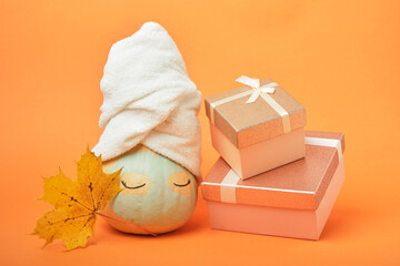A pumpkin smeared with clay with a towel on top and gift boxes on an orange background, the time for holiday gifts and sales concept
