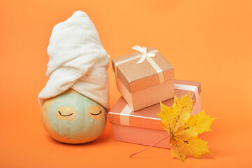 A pumpkin smeared with clay with a towel on top and gift boxes on an orange background, the time for holiday gifts and sales concept