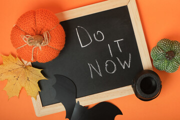 Halloween decor and chalkboard with the inscription "Do it now" on an orange background