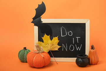 Halloween decor and chalkboard with the inscription "Do it now" on an orange background
