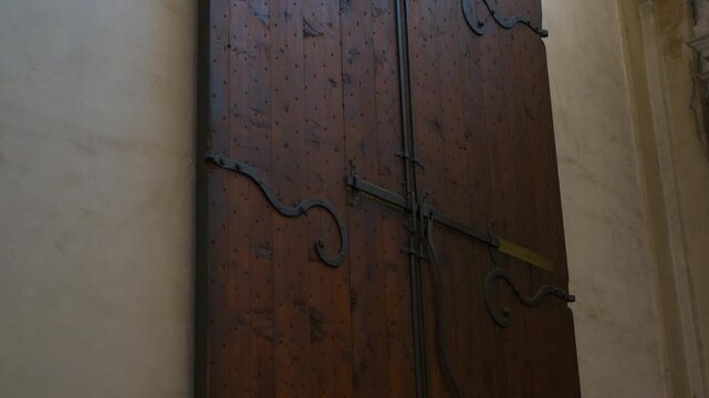 Ancient wooden door with metal hinges in a historical building. Sunlight casting warm glow on weathered wooden door with intricate metal hinges, revealing architectural heritage within structure