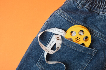 Measuring tape and jeans on an orange background, the concept of fighting excess weight in the autumn period
