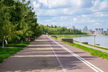 A dedicated bike path, a pedestrian promenade. Scenic riverside pathway lined with trees and city skyline on a sunny day in summer