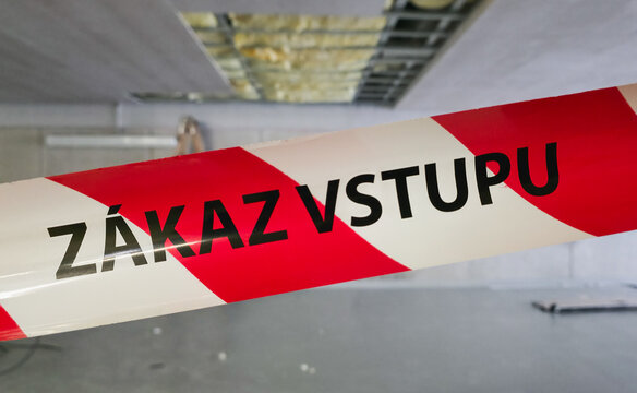 Red and white warning tape with the text Zakaz Vstupu meaning no entry at an indoor construction and renovation site with a blurred background.