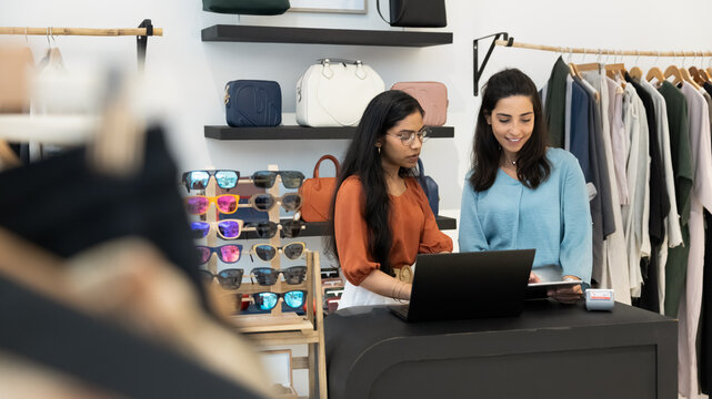 Two retail store assistants working together at checkout counter
