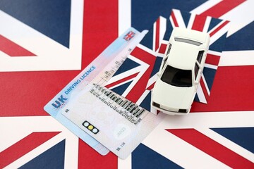 United Kingdom driving license with white toy car on UK flag close up