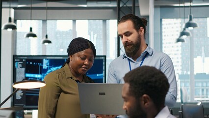Teamworking programmers in office reviewing AI system metrics, monitoring performance dashboards. Tech company coworkers tuning neural networks using tools on laptop, camera A