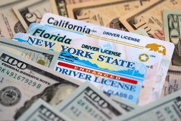 California, Florida and New York state driving licenses among big amount of US dollar bills close up