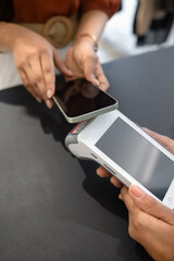 Hands of customer and sales assistant holding smartphone and terminal