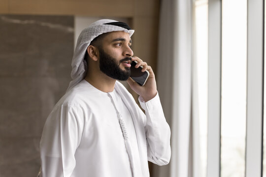 Busy young Arab man in dishdasha speak on phone