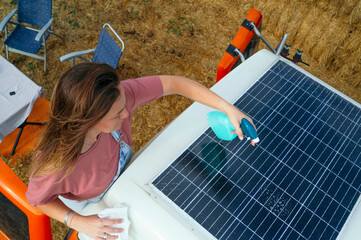 Woman cleaning a solar panel on top of a camper van using a spray bottle and cloth.