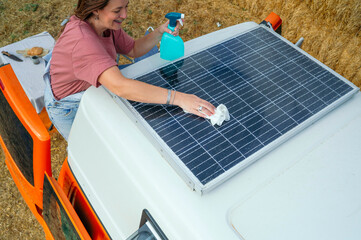 Woman smiling while wiping a solar panel on top of a camper van during cleaning.