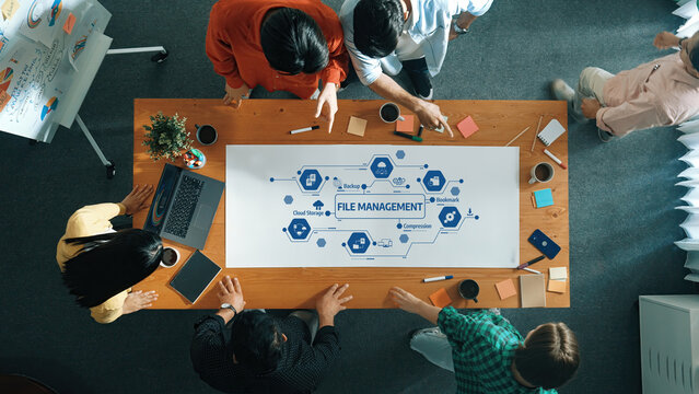 A diverse team engages in collaborative discussion over a file management strategy on a modern workspace table. Overhead view captures their focus on innovative solutions and planning. Amity