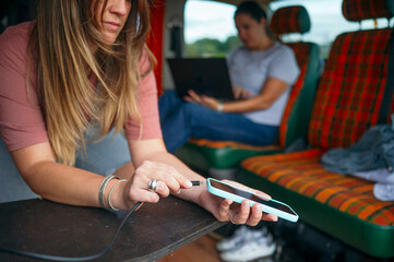 Woman laughing while plugging a charging cable into her smartphone inside a camper van.