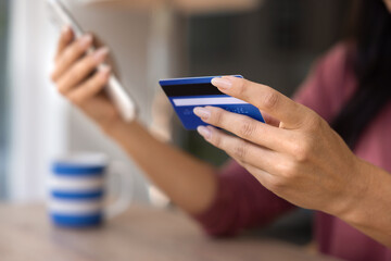 Hand of young woman holding credit card, using mobile phone