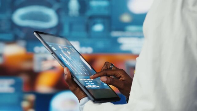 Close up of researcher analyzing human anatomy using tablet app in front of digital health dashboards backdrop. Scientist zooming on touchscreen device display keyboard, analyzing medical scans