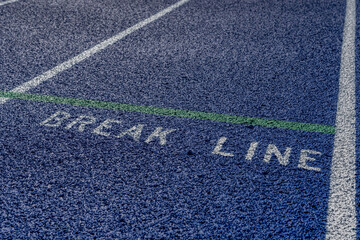 Obraz premium Close up photo of outdoor blue running track with white lane lines, with the word, break line, on a new track.