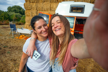 Two women smiling taking a selfie together near orange camper van.