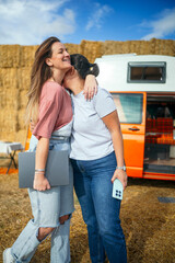 Two women embracing outdoors near orange camper van.