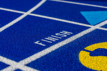 Close up photo of outdoor blue running track with white lane lines, with the word, finish, on a new track.