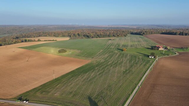 vue a&eacute;rienne panoramique de champs labour&eacute;s en automne avec une for&ecirc;t au feuillage multicolores en fond et unciel bleu au dessus. 
