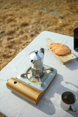 Coffee pot on portable stove with bread and metal cup on table.