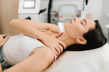 Girl lies calmly beside advanced laser system as a specialist prepares the device for laser procedure. Woman waits for laser procedure before her rejuvenation session.