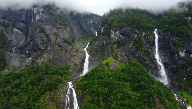 Majestic waterfalls cascade down rugged mountain slopes, shrouded in misty clouds.