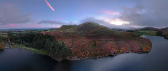 Aerial drone photo of misty hills, colourful fields and calm lake at sunset. Peaceful nature landscape and scenic evening view. Pentland Hills Regional Park, Scotland