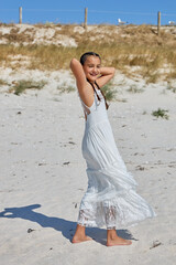 Young girl enjoying a sunny day at the beach while wearing a white dress and playing in the sand with a joyful expression