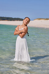 Young girl enjoying summer at a serene beach while playing in calm waters and wearing a white dress