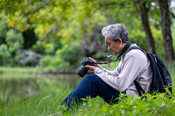 Asian senior man is trekking inside the forest while using camera to take memorable photo for elder exercise outdoor and nature environment therapy concept