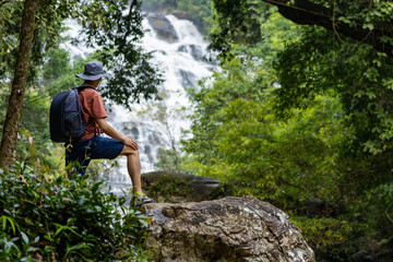 Hiker is trekking in the tropical forest with big waterfall for surveying and discovering the rare biological diversity and ecologist on the field study