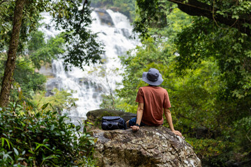 People relaxingly sitting after trekking through tropical woodland with big waterfall for meditation and mindfulness in alternative therapy peaceful forest and listening to soothing nature sound