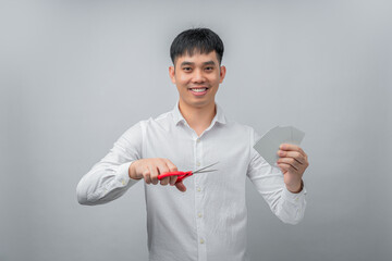 A handsome Asian businessman expresses satisfaction while cutting credit card with red scissors. This concept is suitable for themes of financial freedom, debt reduction, business, and advertising.

