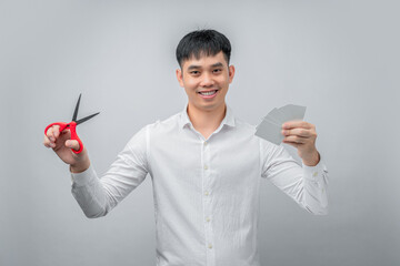 A handsome Asian businessman expresses satisfaction while cutting credit card with red scissors. This concept is suitable for themes of financial freedom, debt reduction, business, and advertising.


