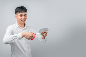A handsome Asian businessman expresses satisfaction while cutting credit card with red scissors. This concept is suitable for themes of financial freedom, debt reduction, business, and advertising.

