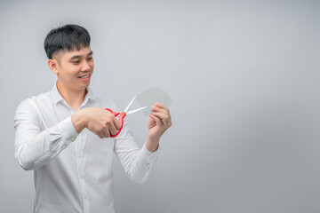 A handsome Asian businessman expresses satisfaction while cutting credit card with red scissors. This concept is suitable for themes of financial freedom, debt reduction, business, and advertising.

