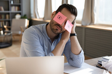 Tired young employee sleeping with funny sticky notes on eyes