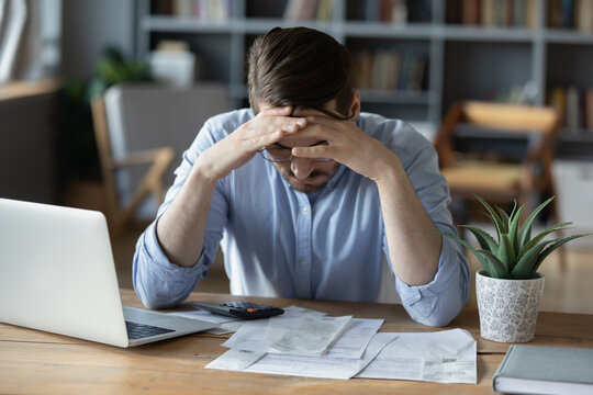 Frustrated young man grabbing head in despair checking finance documents - Powered by Adobe