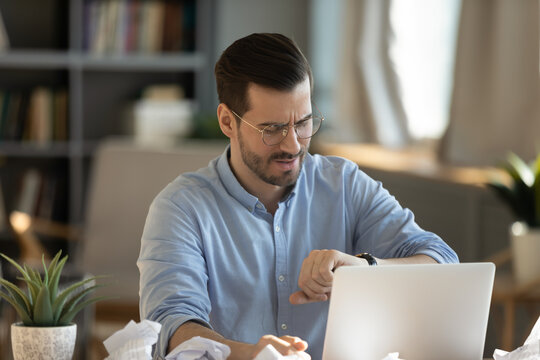 Nervous businessman checking wristwatch at office desk with crumpled documents