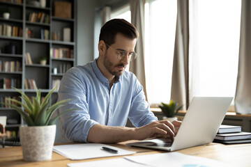 Focused millennial business specialist typing on notebook at workplace desk