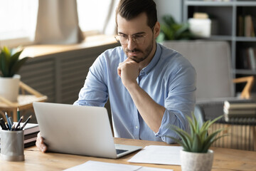Pensive mid adult man office worker looking at notebook screen